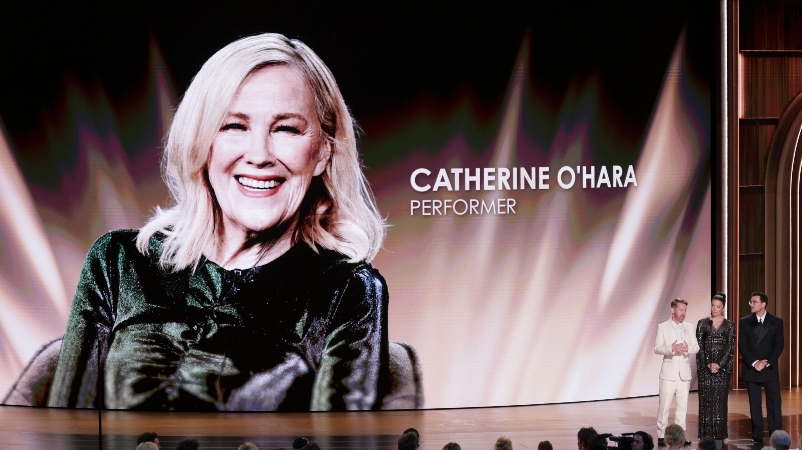 Macaulay Culkin, Annie Murphy and Dan Levy speak onstage next to a big backdrop honouring Catherine O'Hara at the Emmys
