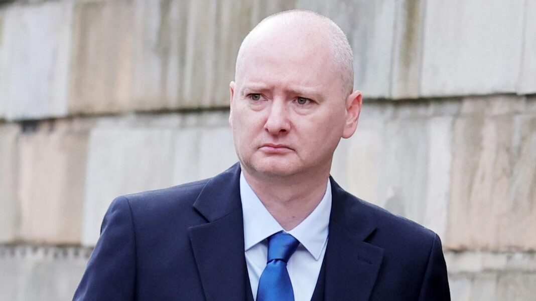 Former world snooker champion Dott jailed for child sexual abuse Person wearing a dark blue suit, light blue shirt, and bright blue tie, standing outdoors in front of a large stone wall. The person is shown from the chest up and looking to the side.