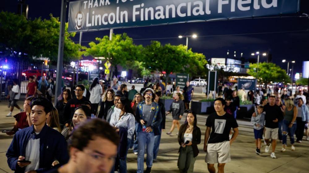 People walk in the evening towards the venue for the concert of pop star Ed Sheeran. A sign above them reads Lincoln Financial Field.