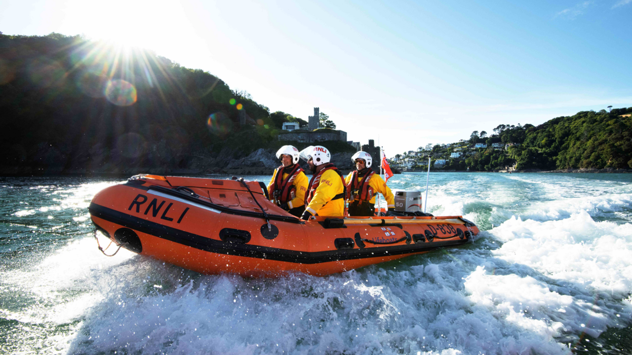 An RNLI boat speeds along the sea coast with three volunteers on board.