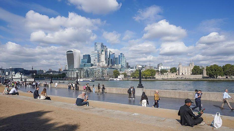 People sit in the autumn sunshine by the London Riverside in London