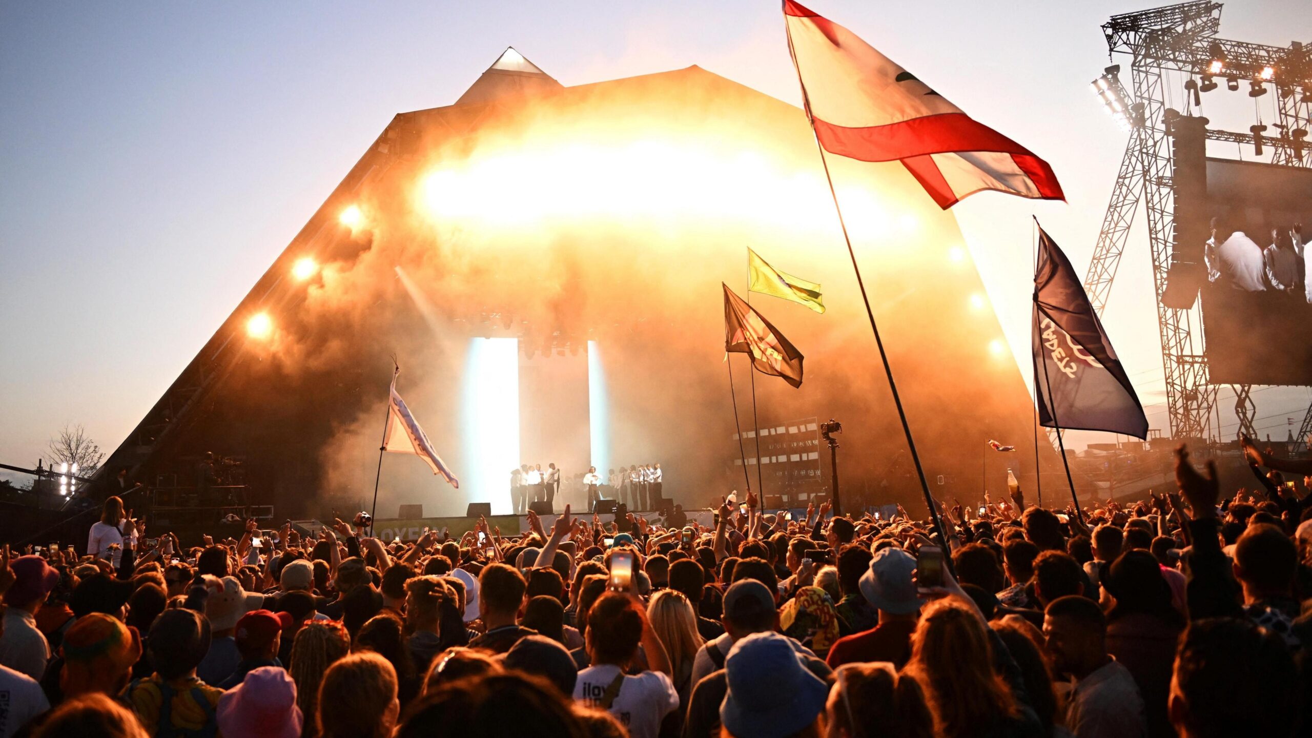 A crowd is standing in front of a stage during sunset.