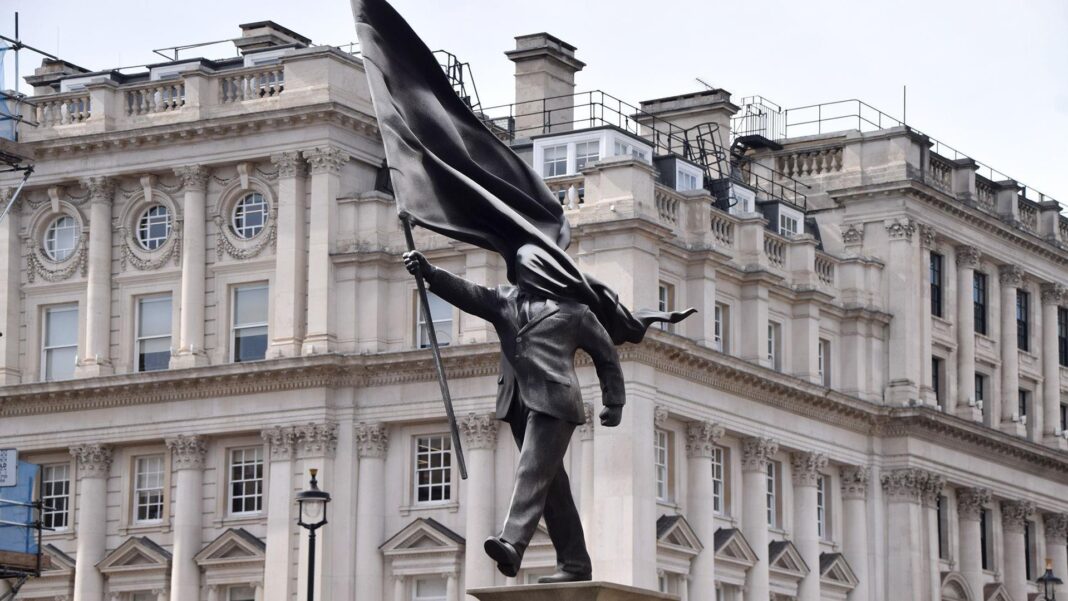 ‘All options’ considered for Banksy’s flag statue A grey statue of a man wearing a suit, walking forward, carrying a flag that covers his face