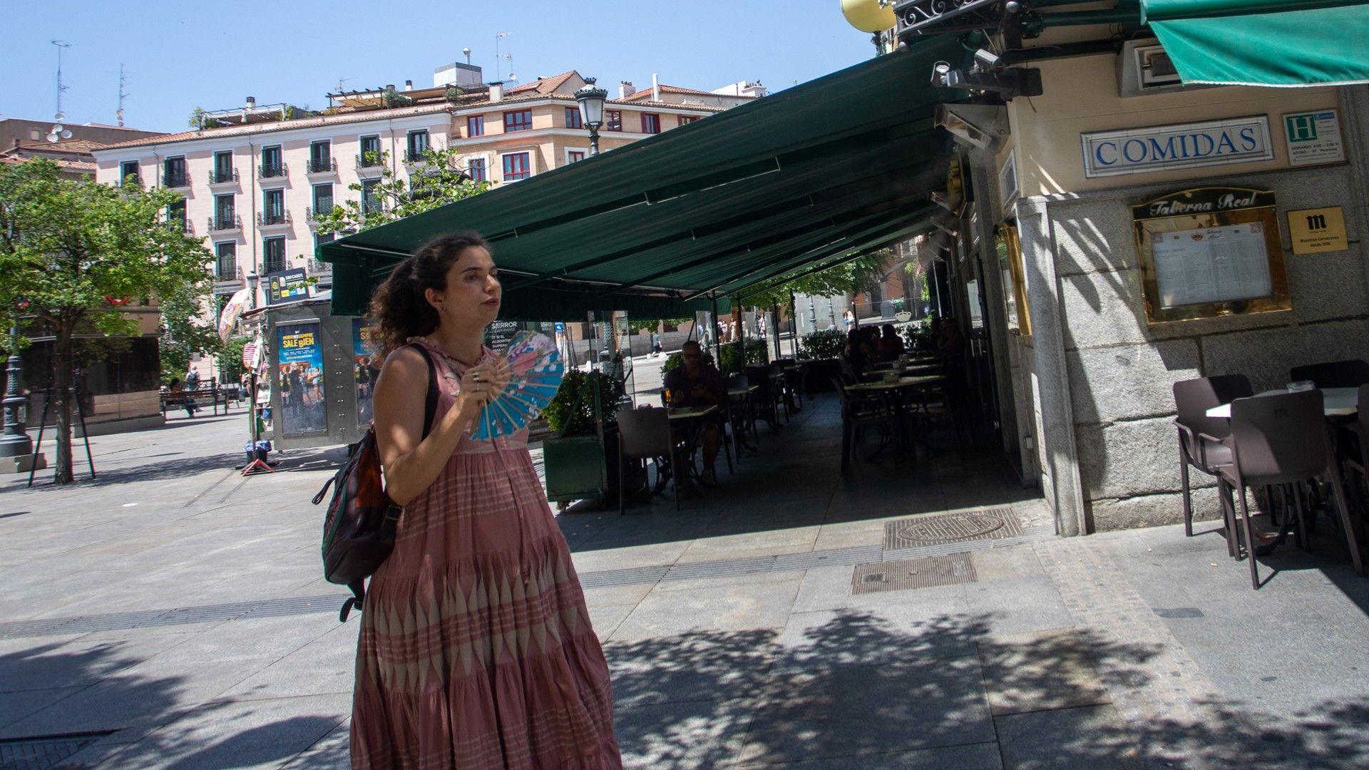 A woman walks through a town square in Madrid, Spain, carrying a handheld fan.
