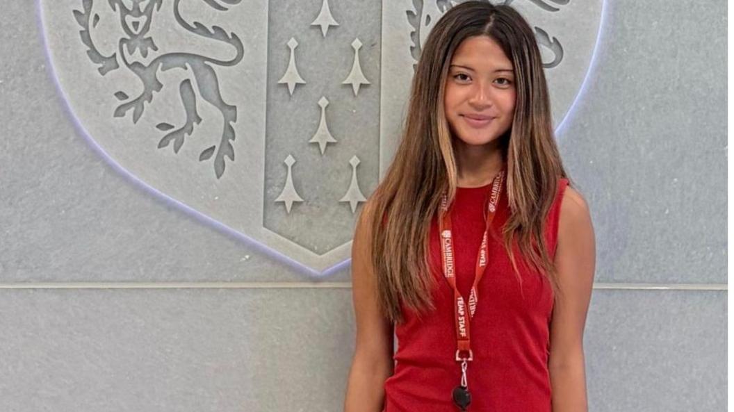 Kiersten is staring at the camera smiling. She has long brown hair that is down and is wearing a red top with a lanyard.