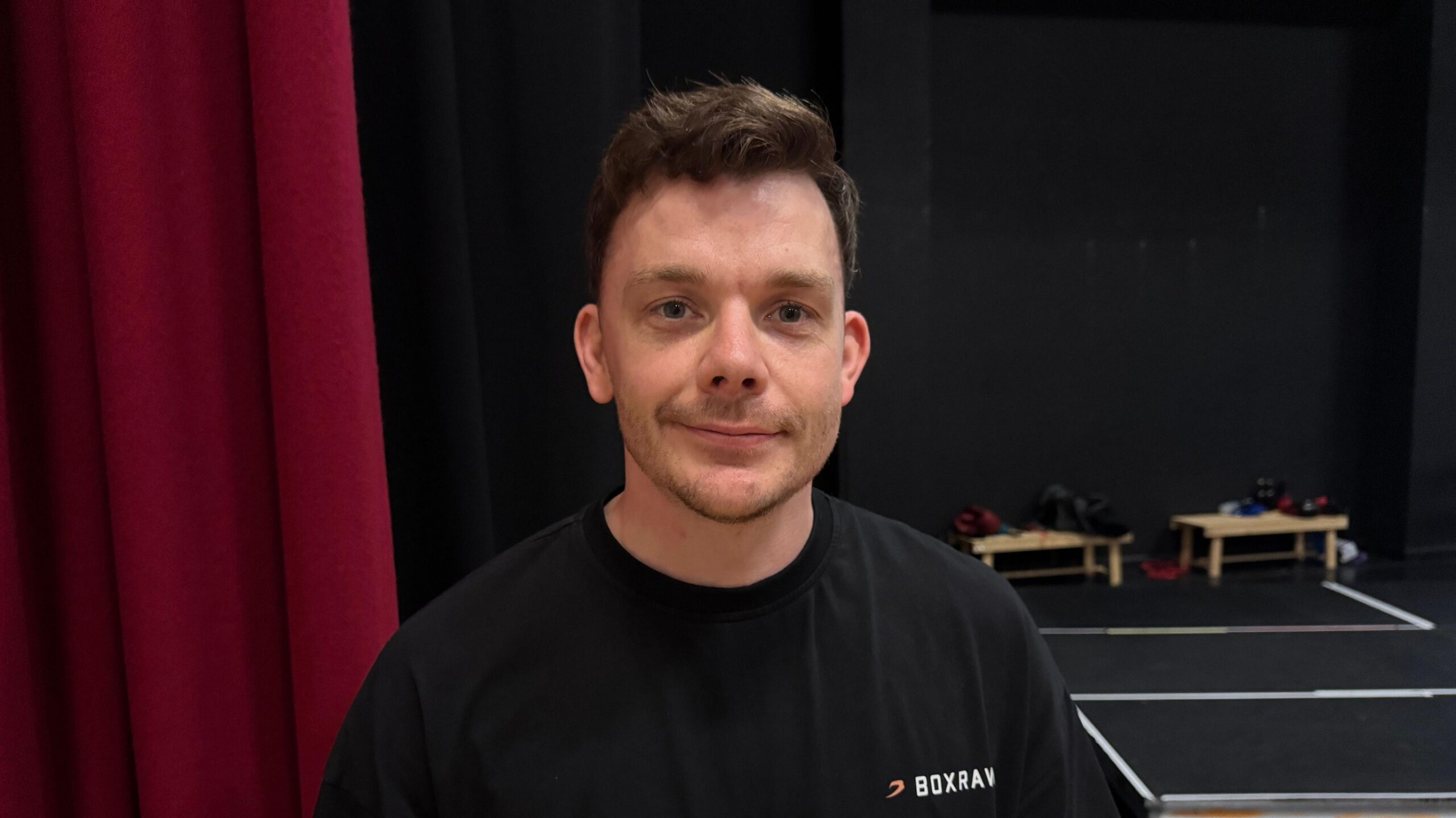 A man looking straight at the camera smilling - he is wearing a black t-shirt.