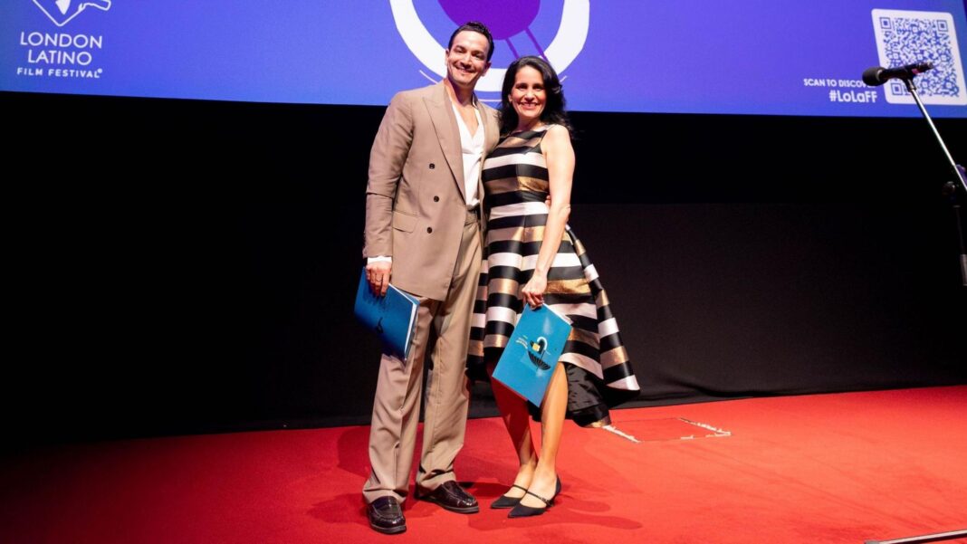 The festival's founders, Cuban dancer Javier Torres and Cuban actress Ketty Rodriguez, stand together on a stage. He is wearing a beige suit, she is wearing a gold, black and white striped dress