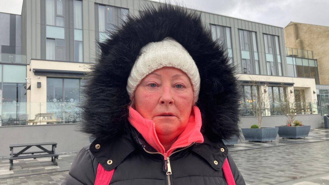‘Dissident republicans may be responsible’ for hotel explosive device – PSNI A woman with a black coat, hood up, wearing a white hat looks at the camera. She has on a pink backpack and stands on a grey-stone street in front of a large grey hotel building