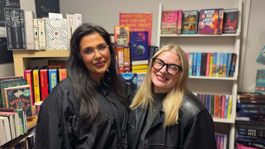 ‘A way to escape’: Fan excitement as new ACOTAR book hits shelves Katie and Amy stand side by side and smile at the camera. Katie on the left has long, dark hair and is wearing a black jacket. On the right, Amy has shoulder-length, blonde hair and is wearing a pair of black framed glasses and a black leather jacket. Both are stood in front of a large bookshelf.