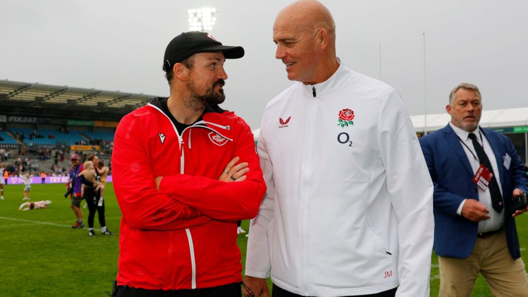 Canada boss Kevin Rouet, wearing a red tracksuit and black baseball cap, and England head coach John Mitchell, in a white tracksuit, face each other while chatting