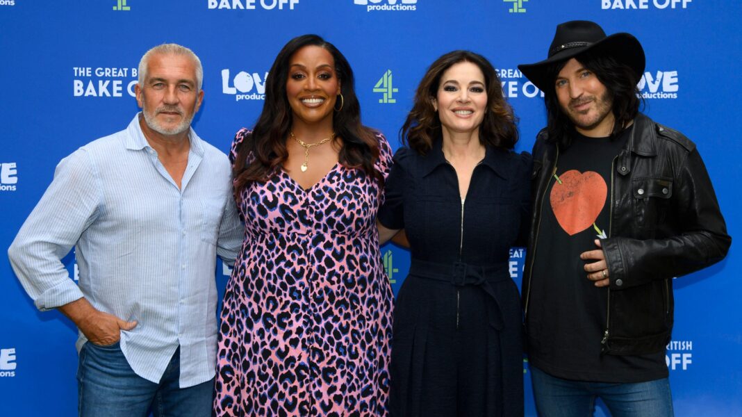 Paul Hollywood, Alison Hammond, Nigella Lawson and Noel Fielding standing in a row with their arms around each other in front of a blue backdrop with Bake Off and Channel 4 logos