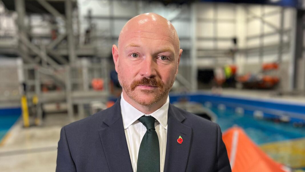 Offshore workers turn to weight-loss jabs to meet helicopter weight rules A bald headed man with a moustache, wearing a tie and dark blue suit. A training facility including a pool is in the background