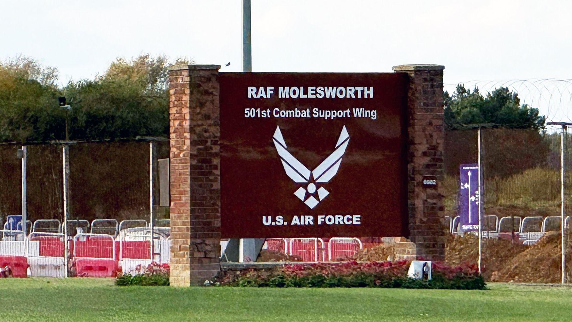 A large brown sign, fixed to brick posts, reads RAF MOLESWORTH and is at the entrance to a military base.