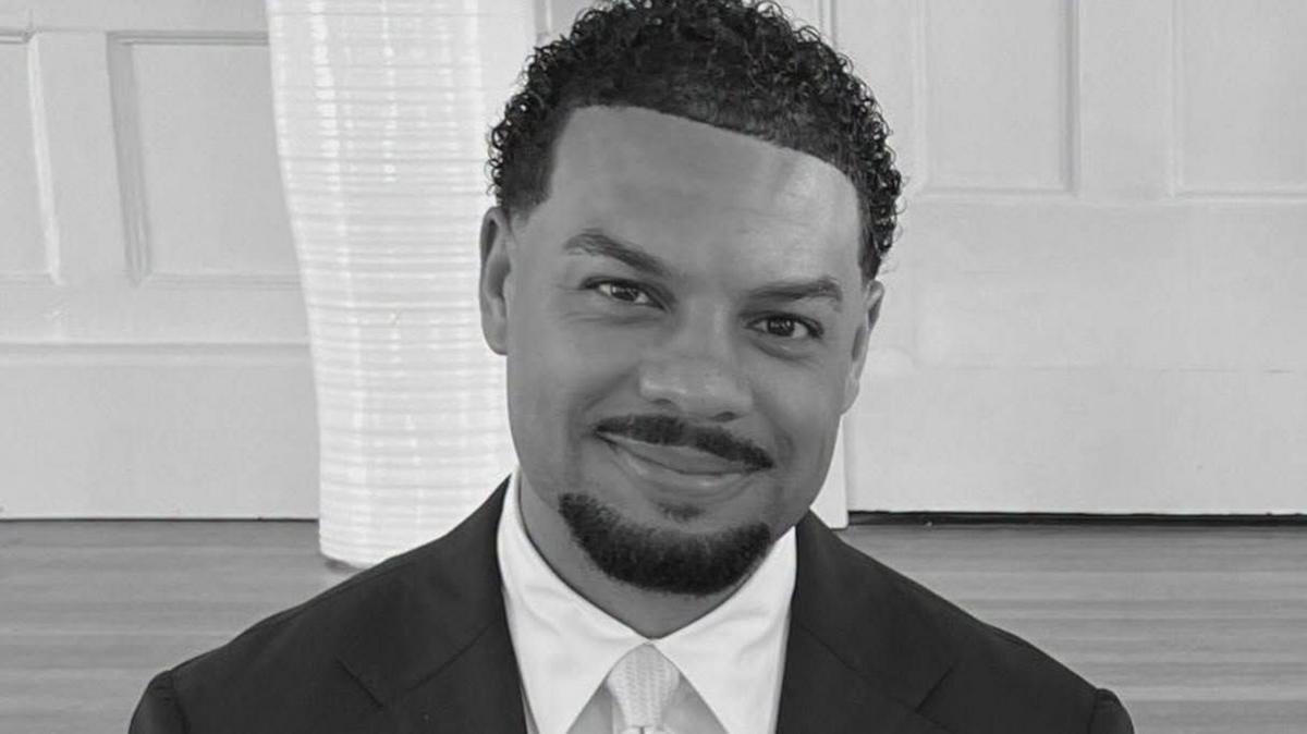 A black and white image of Cassius Newton, who has short, curly hair and is wearing a suit.