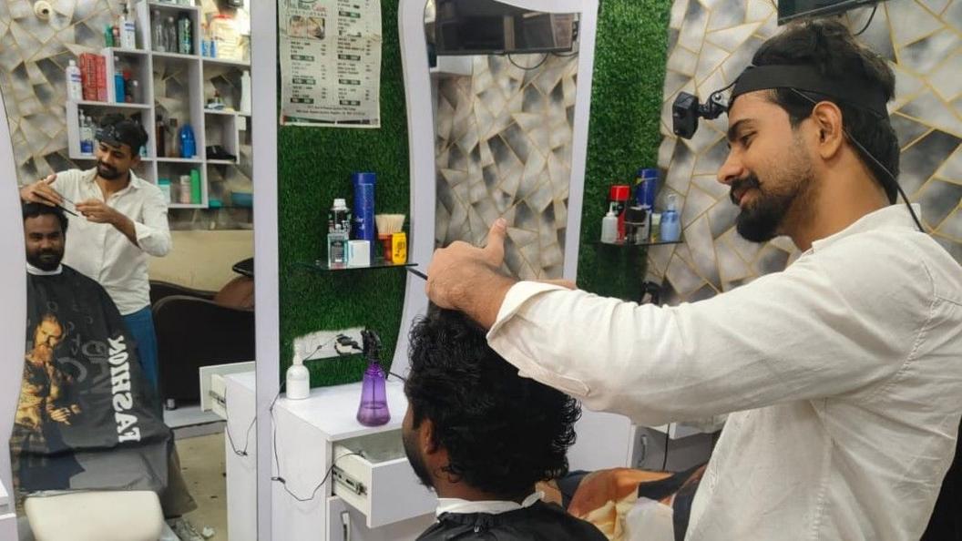 Mohammed Ashim cutting a customer's hair. A headband holds a small camera to his forehead.