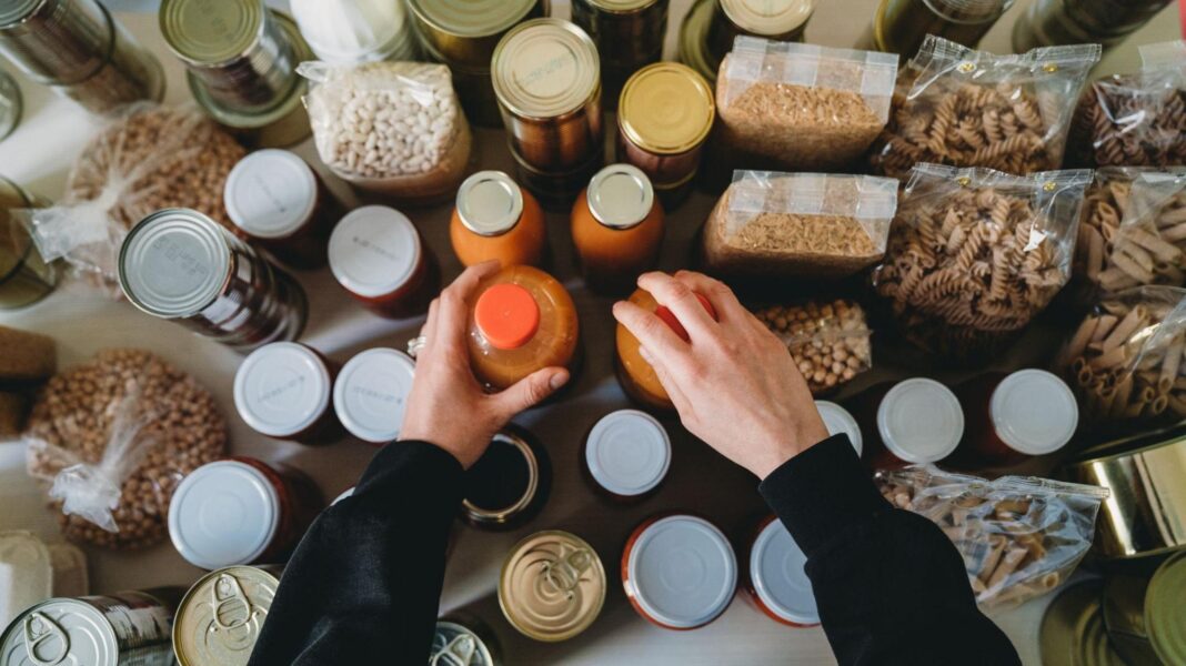 Responsible or panicked? Meet the people around the world already preparing for crisis Woman is rearranging the kitchen pantry. Many cans, bottles and tins on the kitchen table. Panic buying concept.
