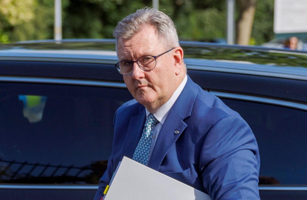 Donaldson has short grey hair and is wearing a blue suit, white shirt and patterned tie. He has round black metal glasses, and is walking in front of a car holding a folder while arriving at Newry Crown Court in Northern Ireland on 8 June.