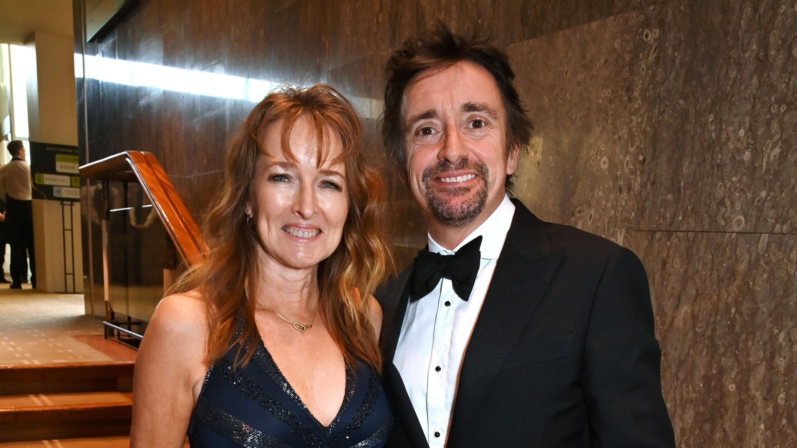 Richard Hammond stood next to his wife Mindy. He is wearing a black tuxedo and she is wearing a black dress, and has wavy red hair.