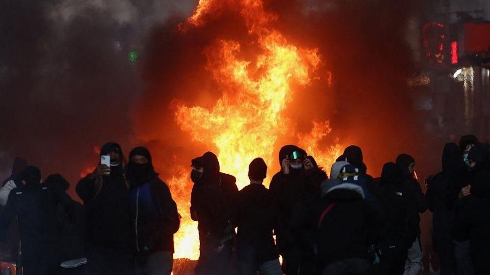 A group of masked people next to a fire burning in Paris