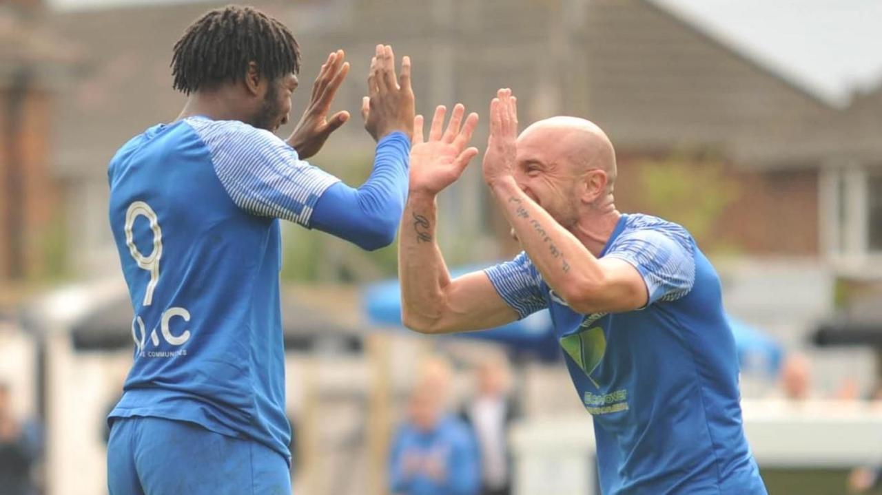 Two men wearing blue football tops high five each other as they celebrate a goal.