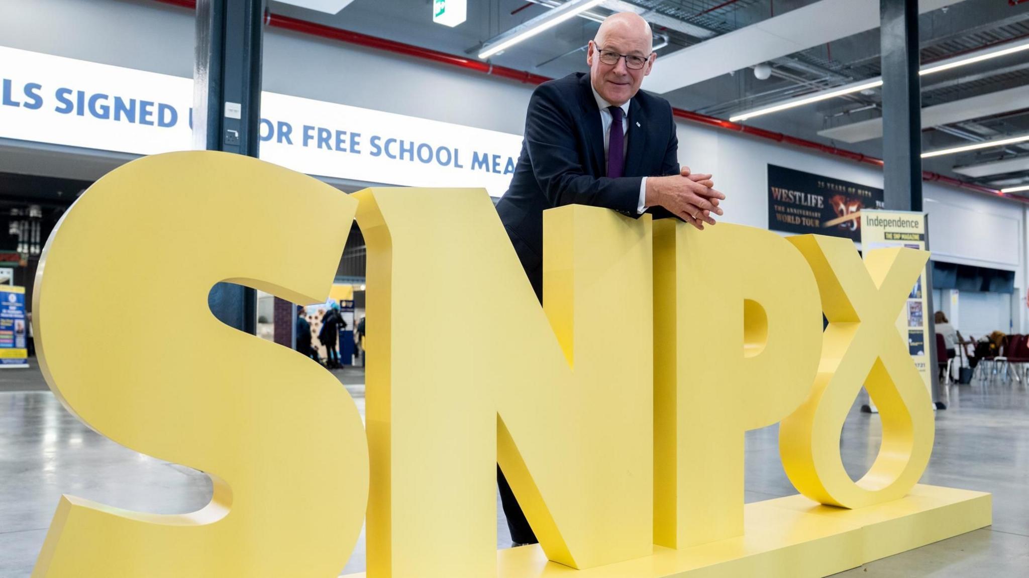 First Minister and party leader John Swinney poses for photographs alongside the party’s logo at the Scottish National Party (SNP) annual conference.