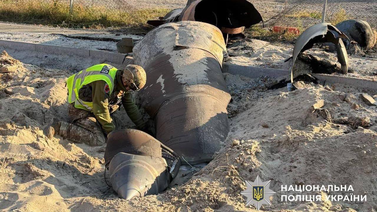 A man in uniform digs in sand beside fragments of what appears to be an unexploded missile.