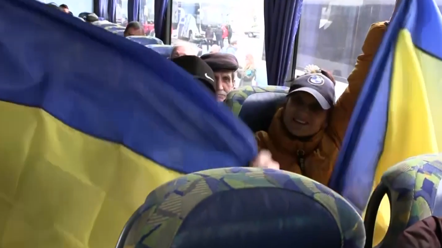 Two people hold up Ukrainian flags on a busy coach full of people