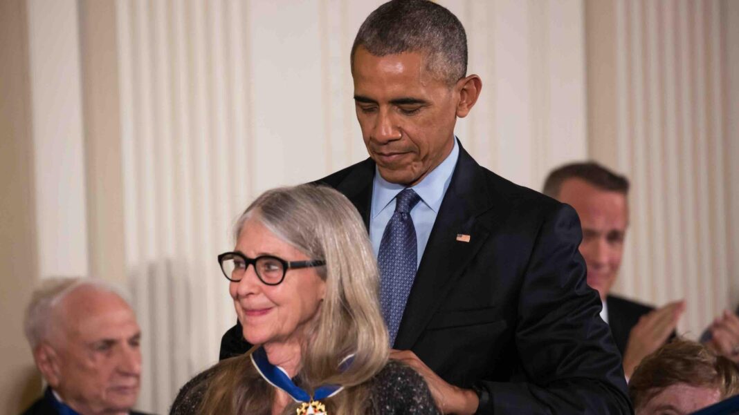 A woman with grey hair being awarded a medal by the-then President Barack Obama, who is placing the blue and gold medal around her neck from behind.