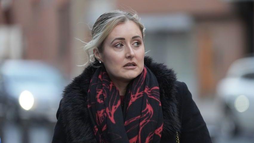 Katie Amess walking down the street wearing a red and black scarf and black coat