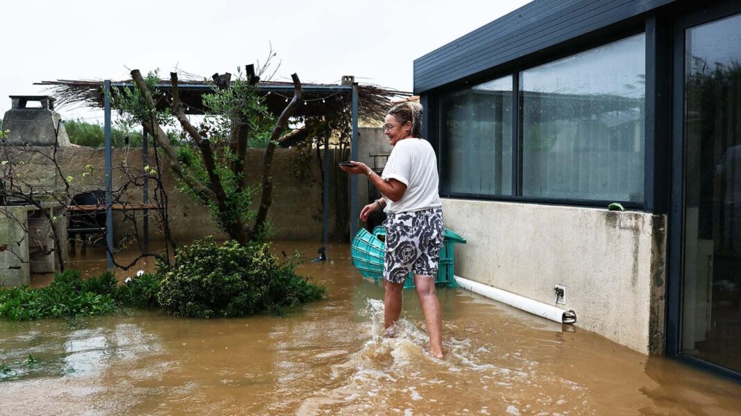 At least four dead after storm brings flooding to southern France A woman wearing shorts and a white t-shirt wades through brown water in front of her house