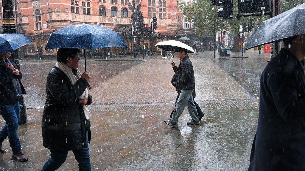 People walking along a street lined with shops with umbreallas in the heavy rain