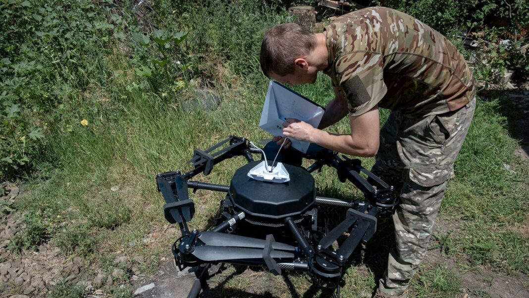 Why Starlink internet is so important on the battlefield in Ukraine A soldier in army fatigues connects what looks like a white ipad to a big black drone in green bushland.