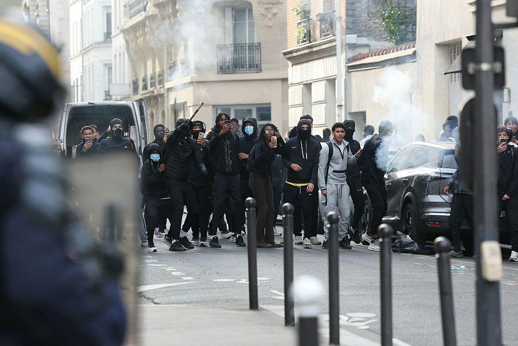 A line of protesters in hoods and face coverings gesture at police on the streets