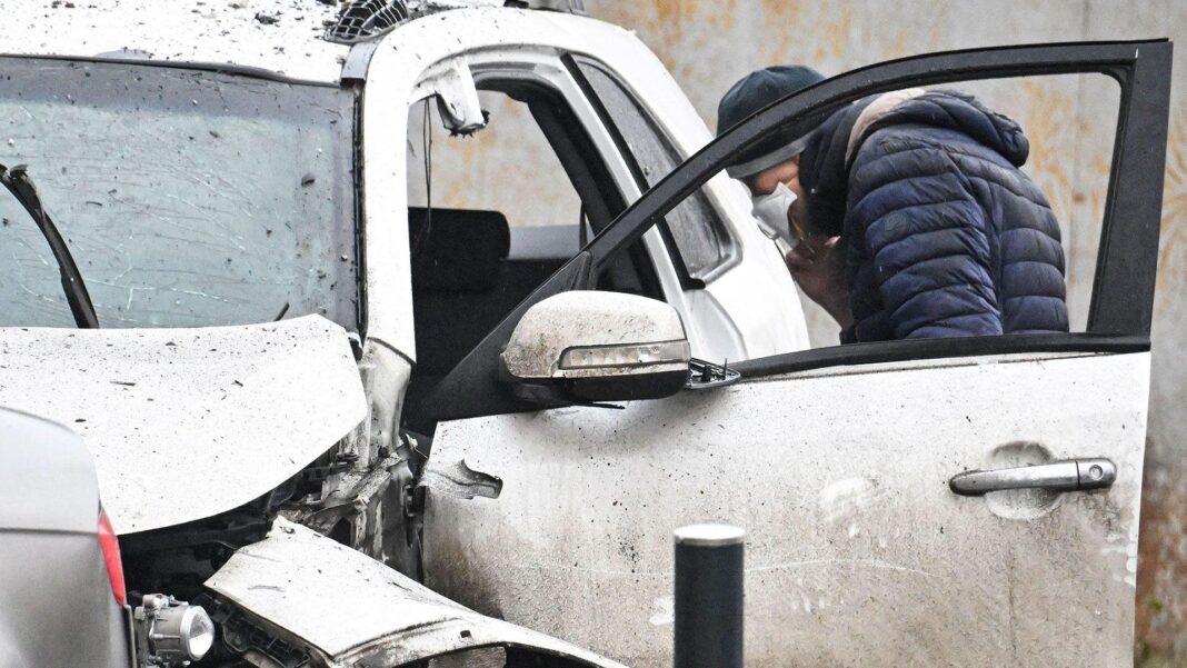 Inside the shadowy world of anti-Putin sabotage from within Russia An investigator wearing a face mask and a blue padded jacket looks into a destroyed car in southern Moscow on December 22, 2025. The car is white and has a shattered windscreen and damage to the roof and bonnet.