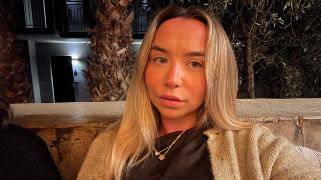 I thought I was dying but it was health anxiety – here’s how to recognise the signs A woman with long blonde hair, she is wearing a beige cardigan, black top and a gold necklace. The background is trees and an apartment complex.