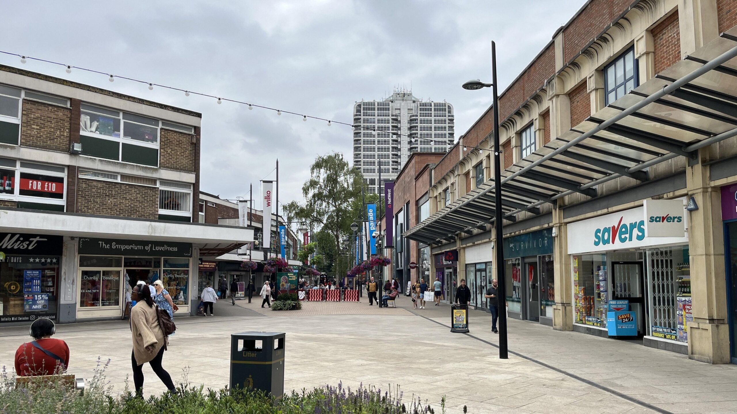 View of Swindon high street, with a beige pavement, lavender planters and a variety of small shops.