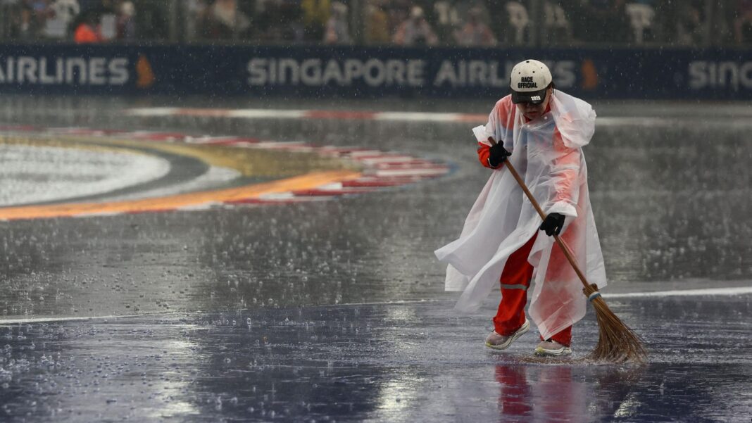 A marshal sweeps the Singapore Grand Prix track as heavy rain falls
