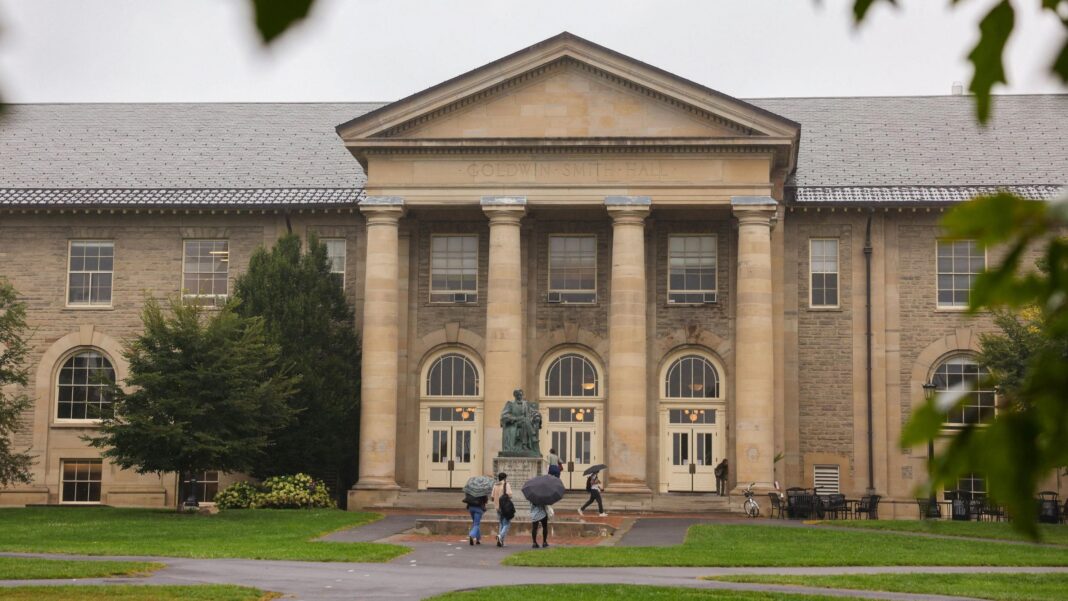 Cornell bans all fraternity parties over gang sex assault allegations Students holding umbrellas walk towards Cornell University, built in yellow stone with four pillars at the entrance.