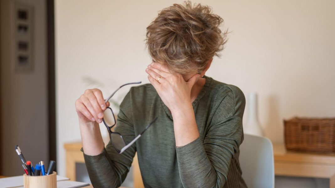Healey to promise £15m to tackle misogyny in Budget A woman sat at a desk rubbing her forehead holding a pair of glasses.