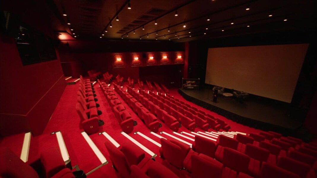 A wide-angle interior view of a 160-seat red velvet cinema auditorium facing a projection screen, with illuminated aisle steps and tiered seating.