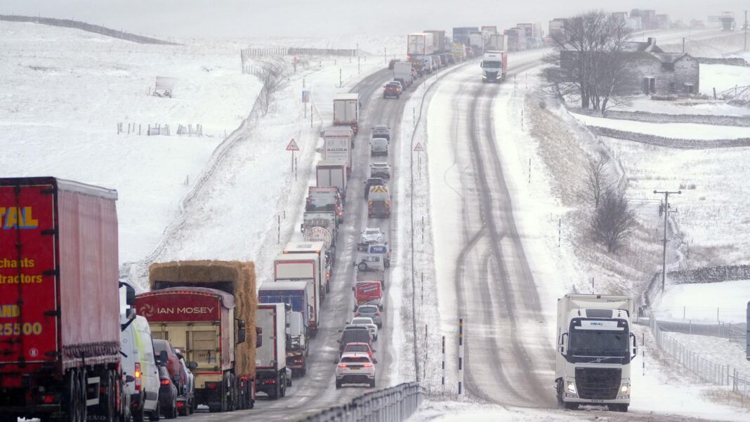 Will El Niño and the polar vortex bring snow to the UK this winter? A road covered with snow and ice with snowy fields on either side, with a queue of cars and lorries in one direction and two lorries moving in the other.