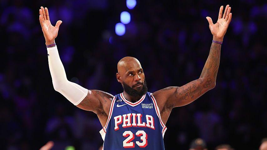 Lebron James, wearing a blue vest with Phila 23 in white text, holds his arms in the air