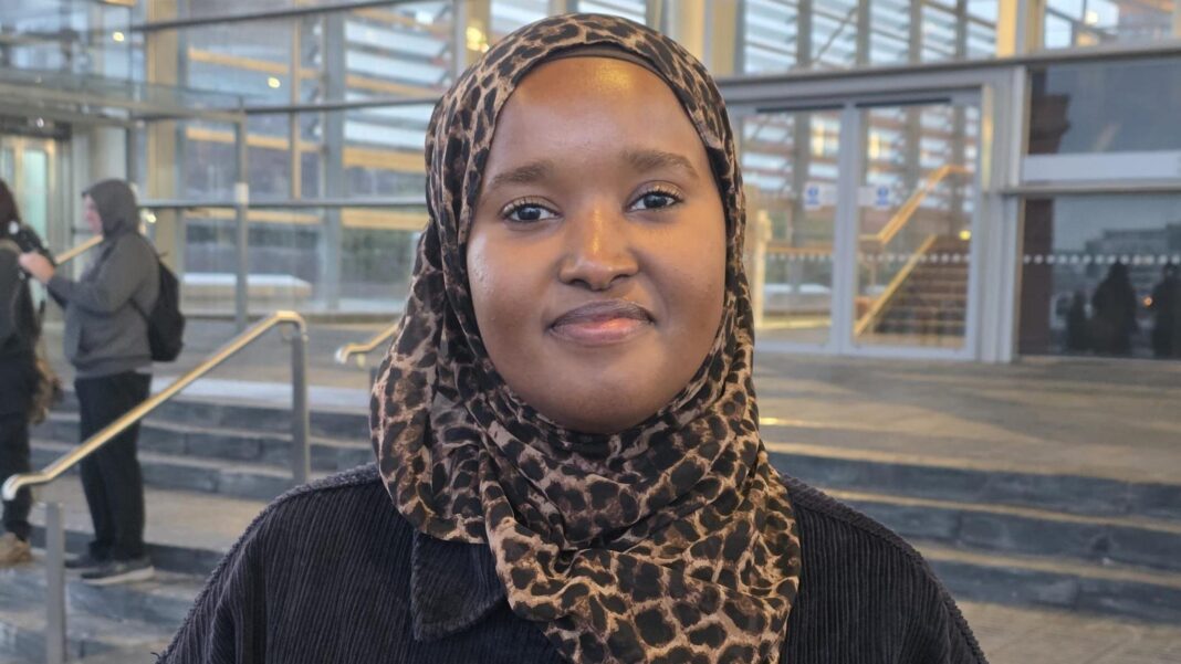 A woman in a leapard print hijab and a blue jacket, on the slate Senedd steps.