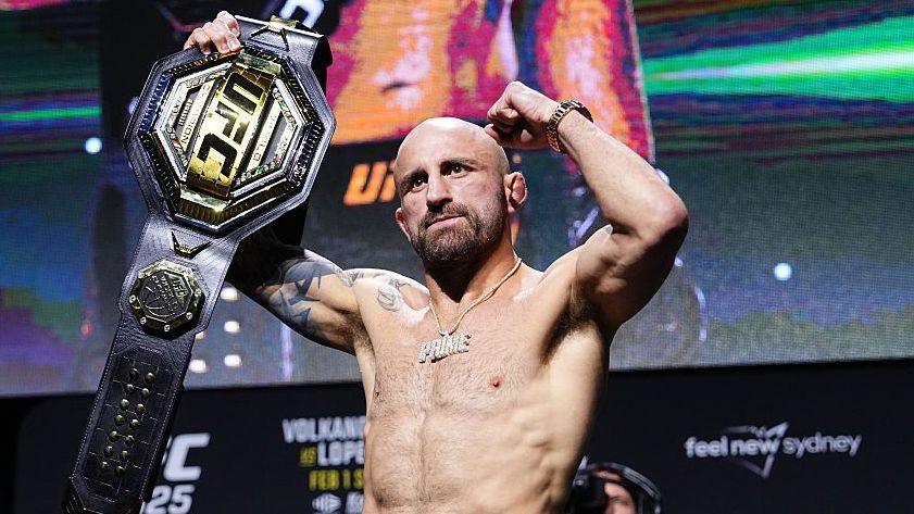 Alexander Volkanovski raises his UFC featherweight title after a news conference