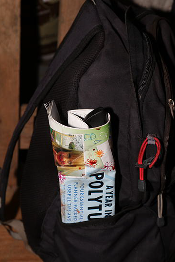 A black backpack, with a flyer poking out of a pocket.