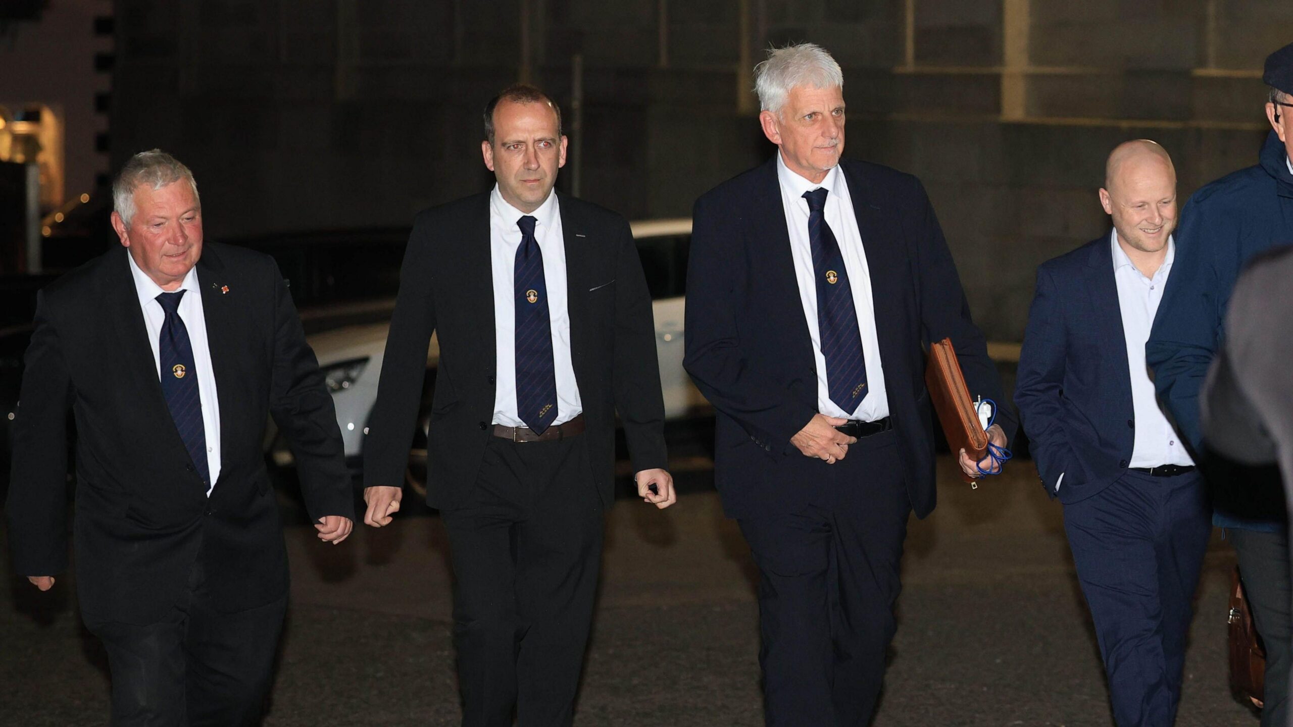 Four men walk together in suits