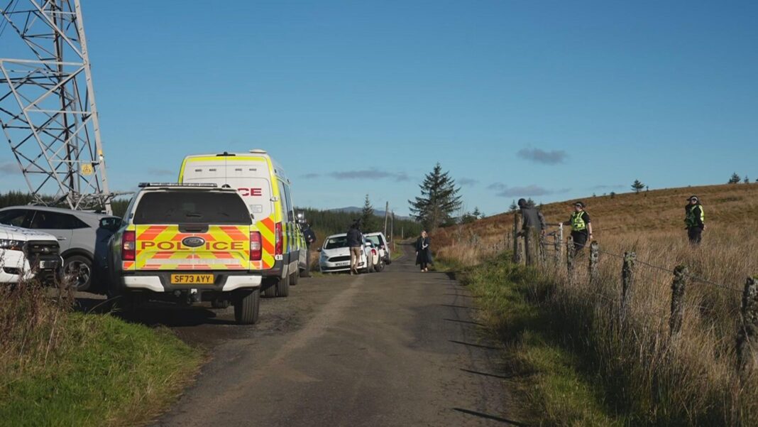 Boy, 16, and 80-year-old man die in light aircraft crash near Loch Lomond A field with a police car and other cars parked along a dirt track road. People walk down the paths and some police officers are in the field