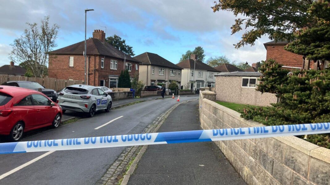 Four murder arrests after teenagers attacked A police cordon blocks access to a residential street lined with semi-detached houses. Blue-and-white police tape stretches across the road in the foreground, while traffic cones and a person can be seen further down the street.