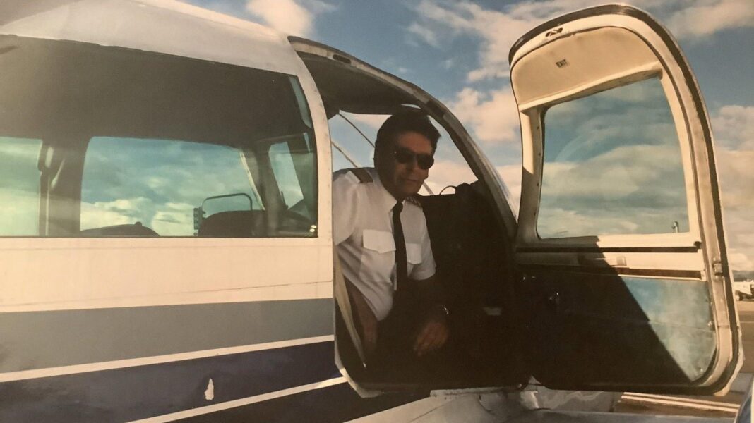 Ian Haggis, wearing a shirt and tie and sun glasses, pictured sitting in a plane