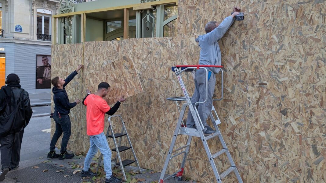 France prepares for day of protest a week after nationwide riots Three male workers, two on ladders, boarding up a shop front on the Champs-Elysees in Paris.